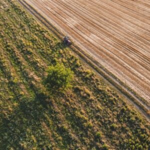 An aerial shot captures a tractor cultivating vast farmland during summer in Berlin, Germany.