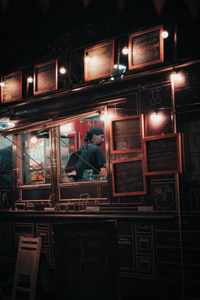 Nighttime food truck scene with illuminated menu and bustling vendor.