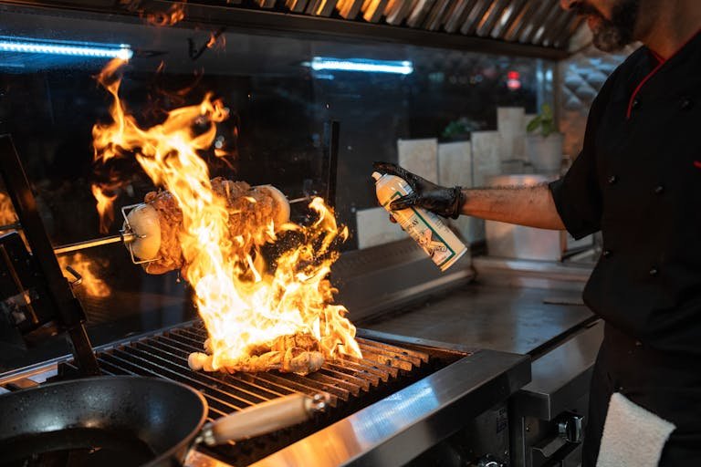 Chef uses a culinary torch to ignite a flaming grill indoors, showcasing dynamic cooking.