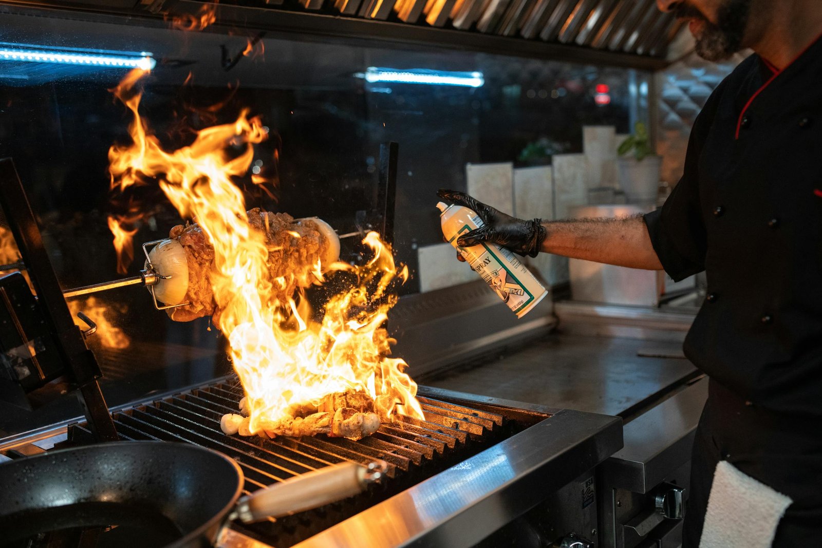 Chef uses a culinary torch to ignite a flaming grill indoors, showcasing dynamic cooking.